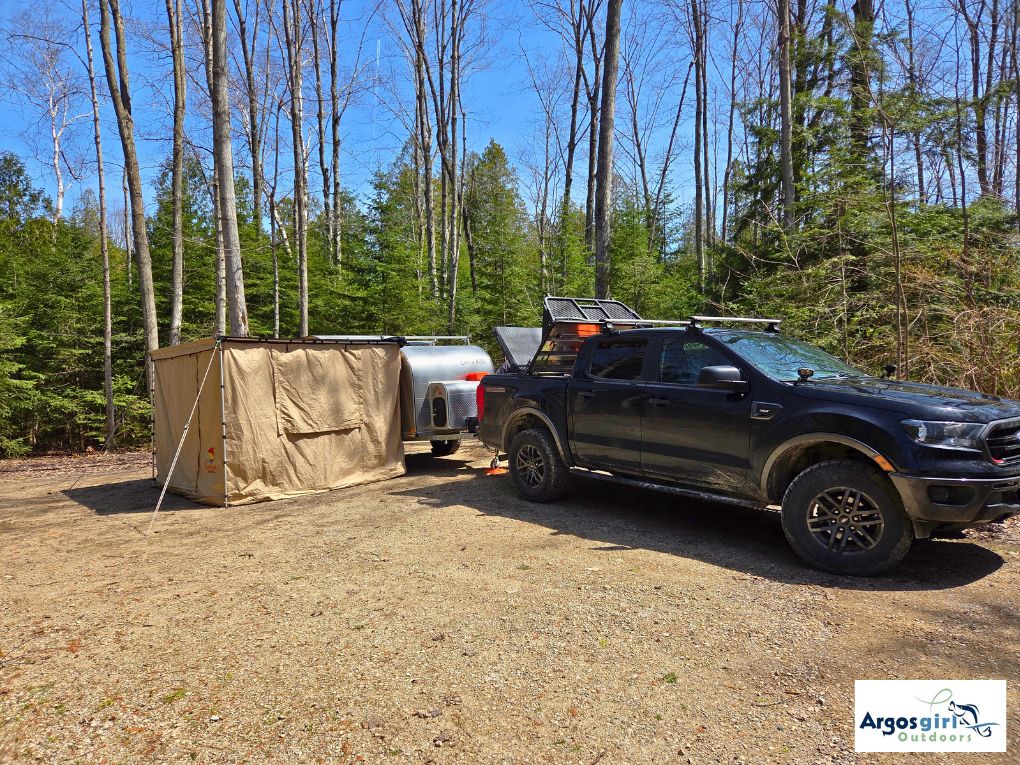 black truck with teardrop trailer and beige side tent at camp site