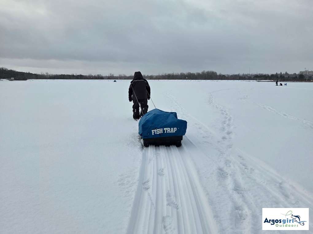 man walking across frozen lake towing ice hut